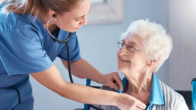 Eine junge Pflegerin hört in ihrer Funktion als Pflegehelferin bei einer Patientin mit einem Stethoskop den Herzschlag ab