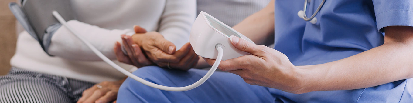 Pflegehelferin misst Blutdruck bei Patientin.