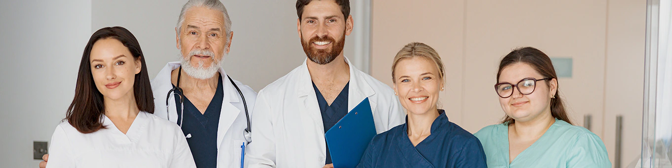 Team aus Ärzten und Pflegekräften lächelt gemeinsam im Krankenhausflur.