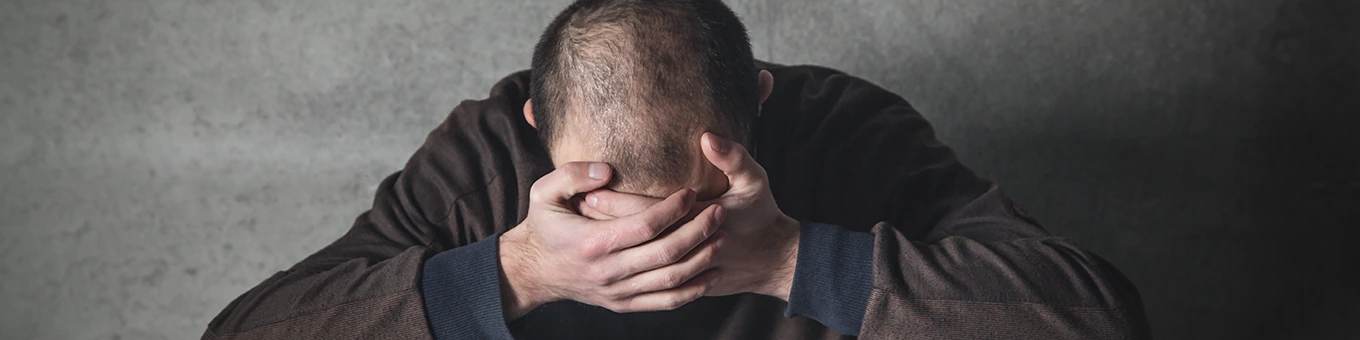 Mann sitzt mit gesenktem Kopf, die Hände halten sein Gesicht.